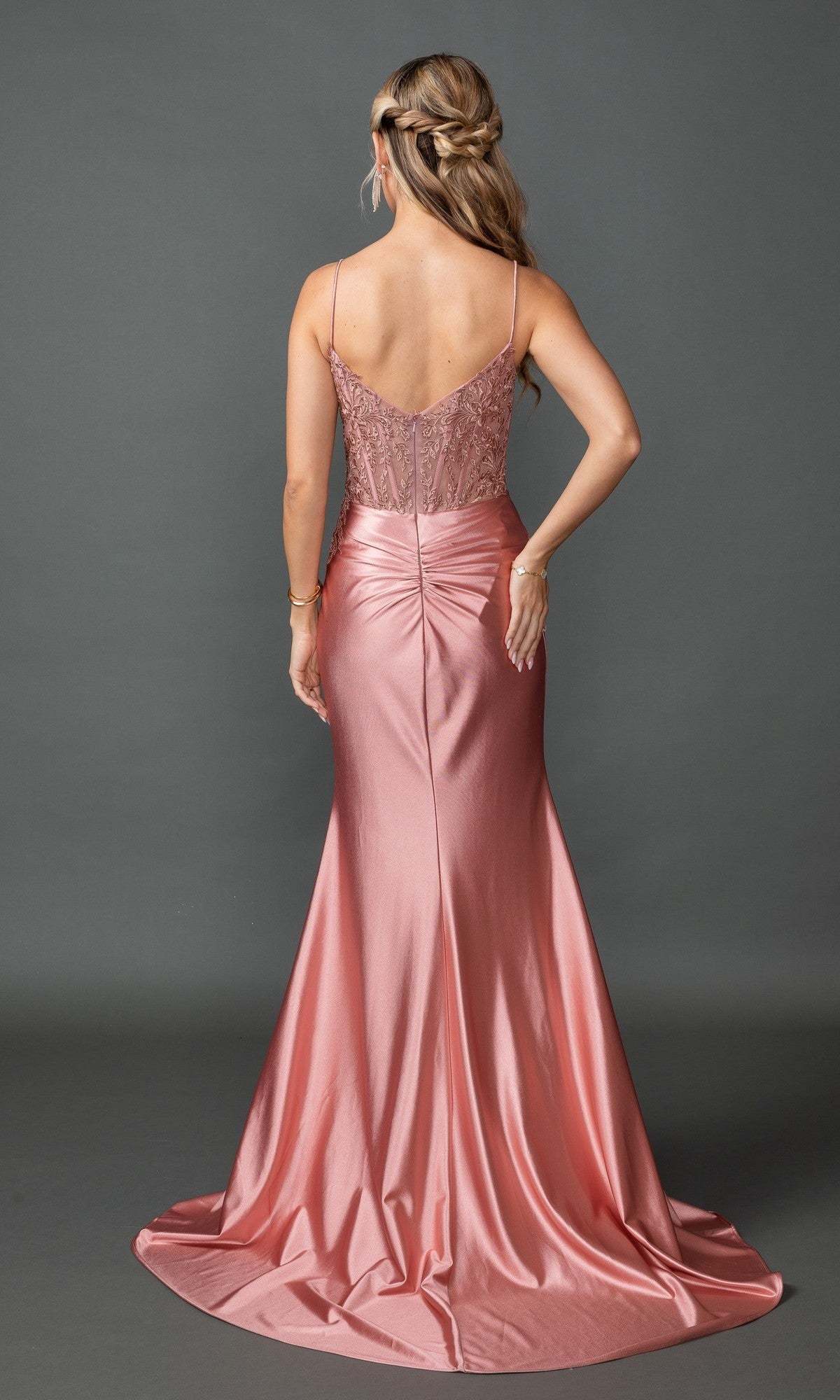 A woman stands facing away, wearing the Sheer-Corset Long Prom Dress: Dancing Queen 4537—an elegant, floor-length pink satin gown featuring thin straps and a fitted, embroidered-lace sweetheart bodice.